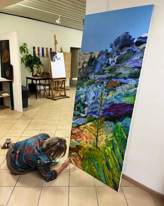 Annemie werkt bij een groot, kleurrijk schilderij in het atelier.