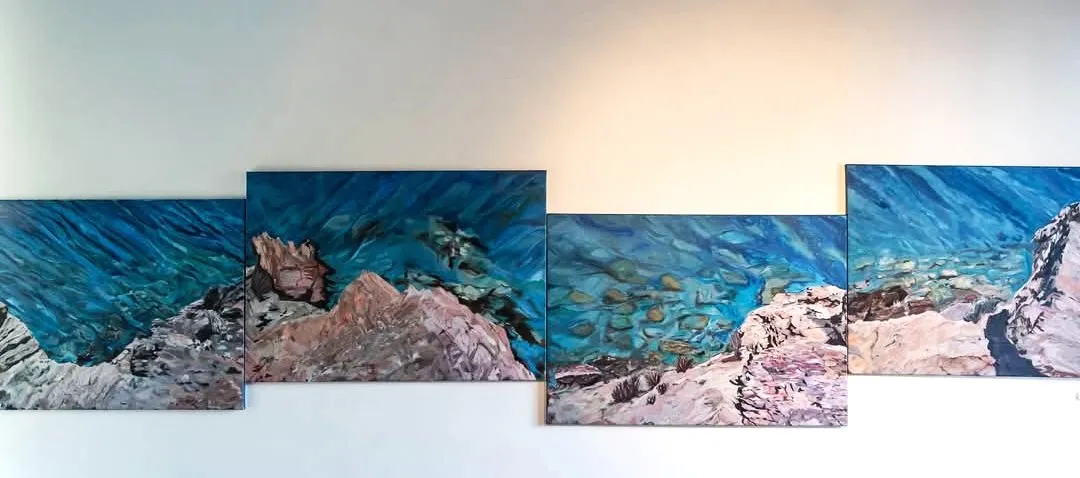 Een meerdelig kustlandschap met blauwe zee en rotsen, tentoongesteld aan een witte wand.